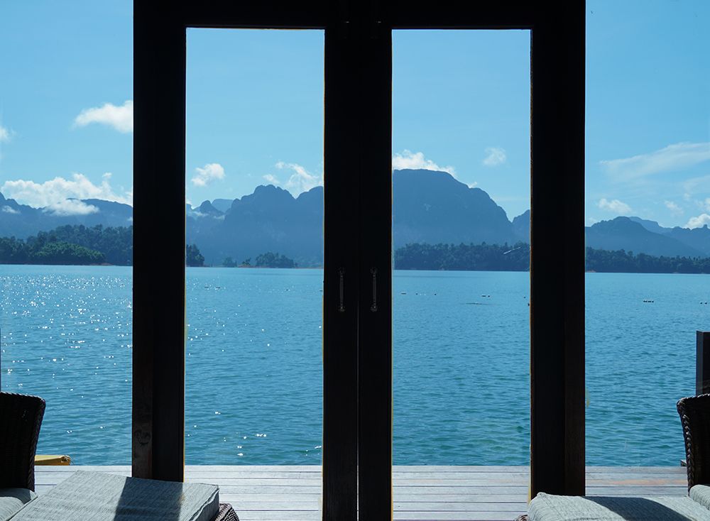 A view from inside a dark room, looking out through tall doors to bright water and mountains